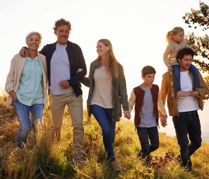 Une famille (y compris les grands-parents) marchant dans les dunes avec le soleil couchant derrière eux. 