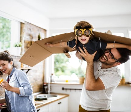 La famille joue comme si le garçon était un avion avec des ailes en carton. 