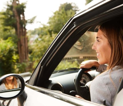 Vrouw die in spiegel van haar auto kijkt.